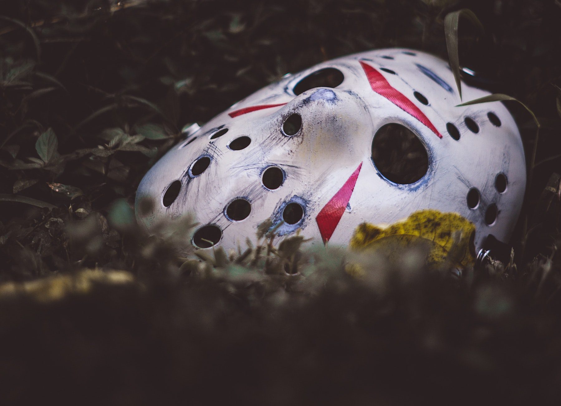 A scuffed and dirty hockey mask similar to that worn by Jason Vorhees, discarded among some leaves.