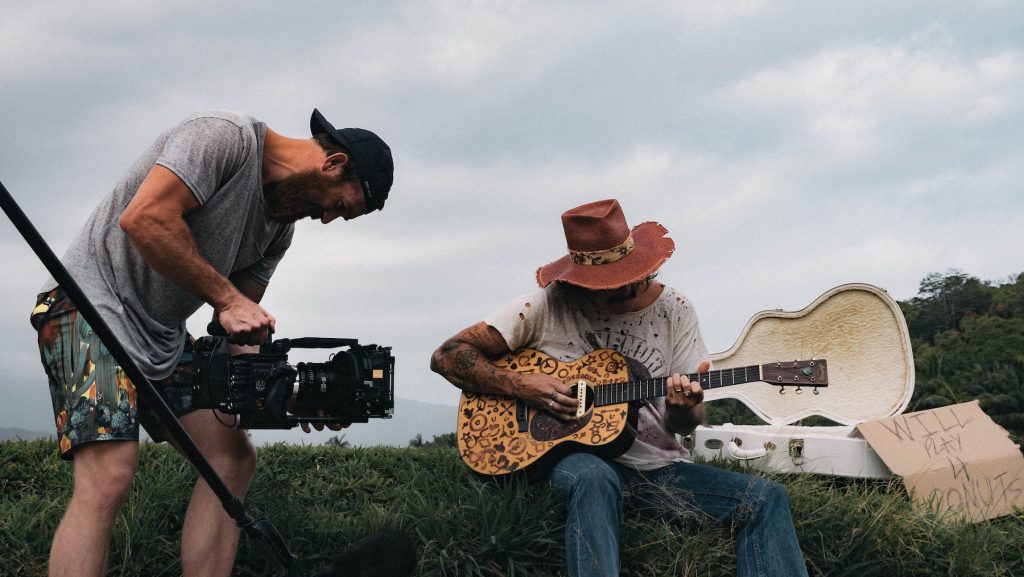 A cameraman gets a closeup shot of a guitarist in a cowboy hat for music documentaries.