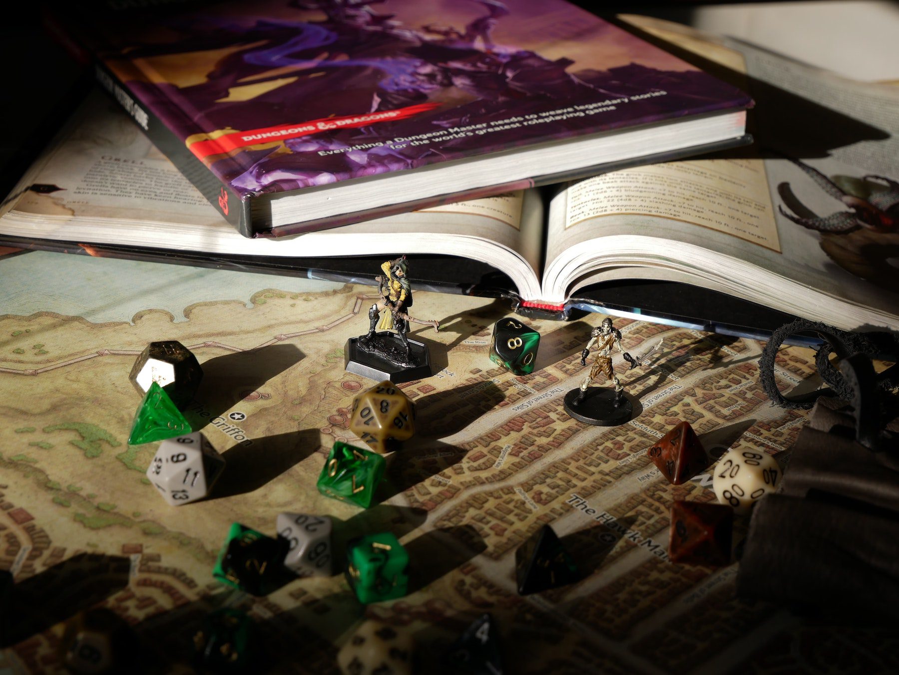 Several D20 dice scattered on a tabletop near some Dungeons & Dragons guidebooks, all producing heavy shadows from unseen light source.