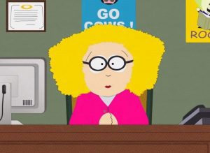 Principal Victoria from South Park sitting behind a desk.