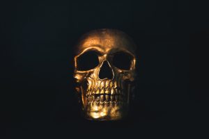 A skull painted gold shrouded in shadow against a black background.