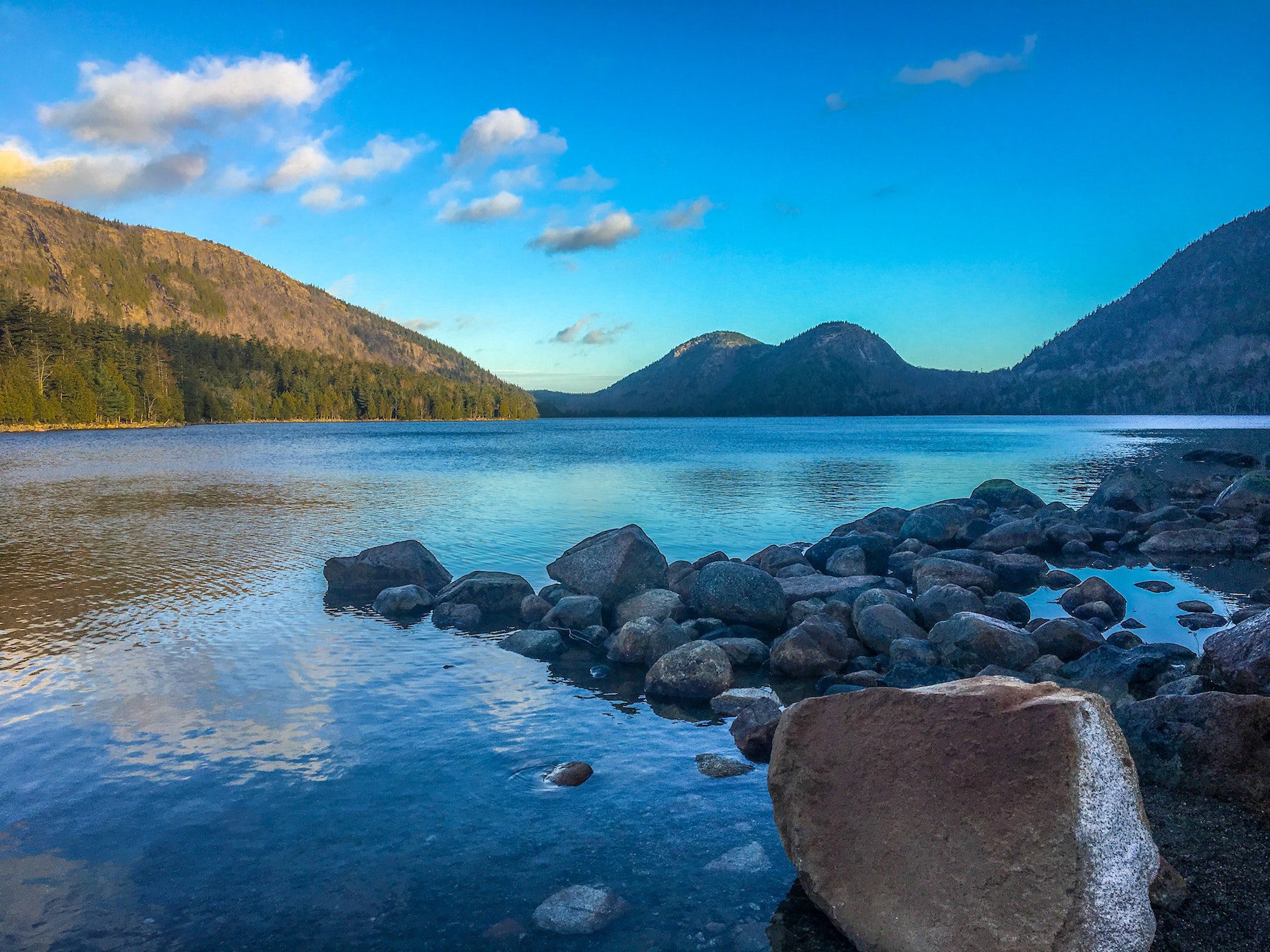 Bright blue waters of Jordan Pond at Acadia National Park with tree-lined hills surrounding the body of water.